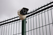 © codorniz - A CCTV surveillance camera on an iron fence against the background of clouds. Close-up.