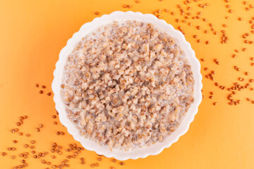 Wall Mural - Buckwheat porridge with milk in a white bowl (plate) on an orange background. Porridge for a child (baby). Healthy breakfast.