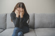 © Pormezz - Unhappy anxiety young Asian woman covering her face with knee on the sofa in the living room at home.