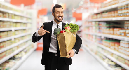 Wall Mural - Bussinesman holding a paper bag with groceries and pointing in a supermarket