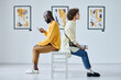 © AnnaStills - Young couple sitting on chair back to back and resting after excursion at art gallery