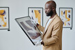 © AnnaStills - African guide examining modern art in his hands while working at art gallery