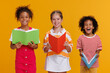 Group of cheerful happy multinational children with books on  yellow background