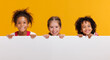 © JenkoAtaman - Group of cheerful happy multinational children with blank white poster on  yellow background