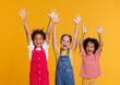 © JenkoAtaman - Group of cheerful happy multinational children shout with joy raising his hands up on  yellow background