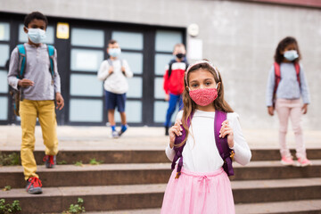 Wall Mural - Portrait of schoolgirl in medical mask standing on the street, kids on background