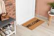 © New Africa - Doormat with word Welcome near shoe rack on white wooden floor in hall