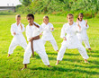 Barefoot kids doing kata during outdoor karate training.