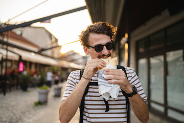 One man young adult modern caucasian male in the city in sunny day walk and eat sandwich fast food concept urban life copy space tourist eating on the street real person