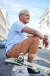 Relax, skateboard and city black man in street of California in summer with Gen Z fashion. Edgy, young and trendy African American skater male in the USA resting on urban road with smile.