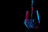 Fototapeta Na ścianę - Water highlighted in blue and red splashing into a glass