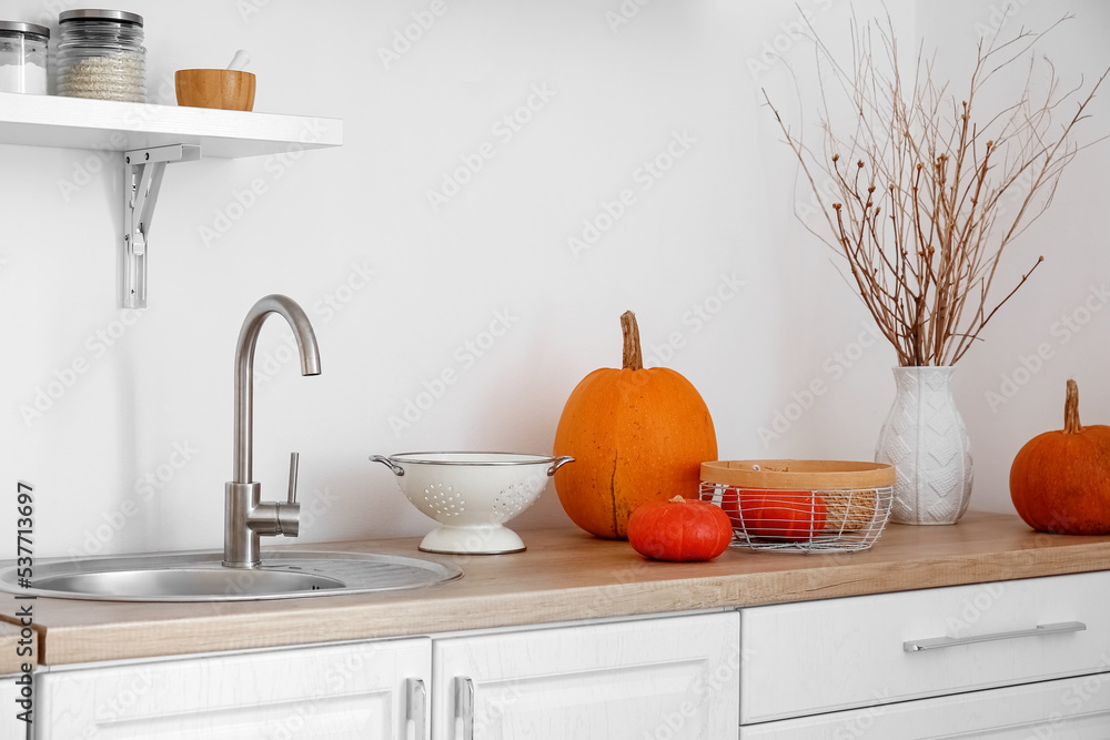 Basket with Halloween pumpkins and colander on counter in kitchen