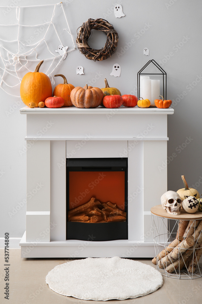 Modern fireplace with pumpkins, table and Halloween decor near light wall