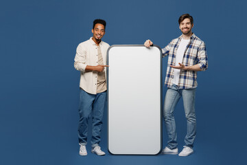 Wall Mural - Full body young two friend men wear white casual shirt together show point finger on big huge blank screen mobile cell phone smartphone with mockup area isolated plain dark royal navy blue background