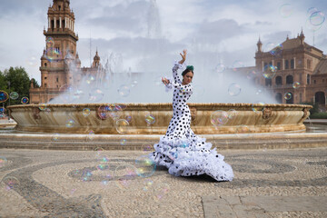 Sticker - Young teenage woman in white suit with black polka dots, dancing flamenco in front of water fountain and surrounded by soap bubbles. Flamenco concept, dance, art, typical Spanish dance, bubbles.