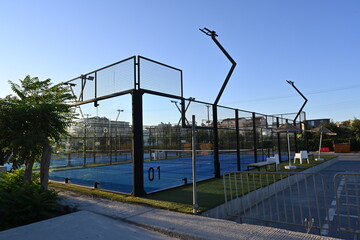 An enclosed blue court for padel with construction created by mesh and the glass back walls. Padel is a racket sport played in doubles and is similar to tennis with the same rules of scoring.