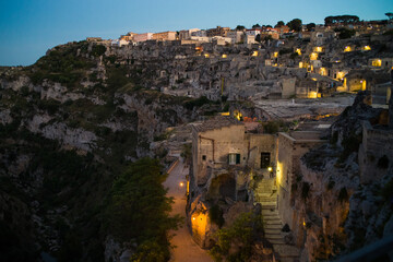 view after dark of old stone houses and churches on the slopes of the gorge in the historic center of the old town of Matera illuminated by street lamps. Cascade buildings of the old town with rocks 