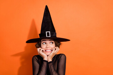 Wall Mural - Photo of charming young lady look empty space frighened bite nails wear stylish black halloween witch clothes isolated on orange background