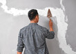 © Meeko Media - An Asian man smooths plaster over cracks in wall with a trowel home fix DIY