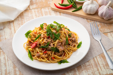 Wall Mural - Stir fried Spaghetti with Canned tuna fish and crispy basil leaves in white plate,Spicy pasta Pad Kra Pao.Thai fusion food