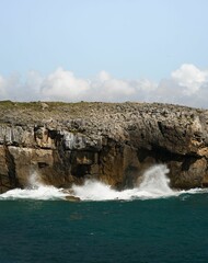 Vertical shot of the coastline with waves crashing against the coast with clouds in the background