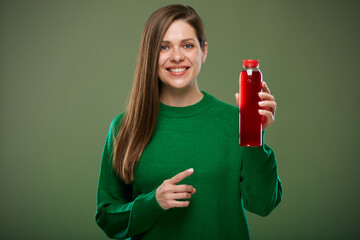 Wall Mural - Smiling woman holding bottle with red juice and pointing finger. Isolated advertising portrait on green.