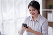 © David - Image of smiling attractive and charming asian woman using mobile phone while working on laptop in modern office