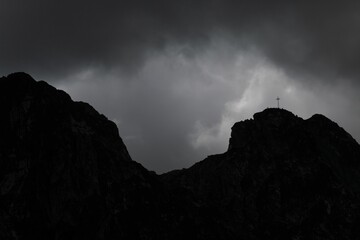 Wall Mural - Grayscale shot of a cross on a mountain with a gloomy cloudy sky background