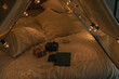 Gifts on camping tent bed decorated with Christmas lights. Kid's bedroom. Winter holidays. Evening atmosphere.