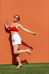 Wall Mural - Girl on an orange background in red glasses. Cheerful girl, advertising shooting