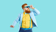 © Studio Romantic - Fat young man in funky modern outfit having fun at disco party. Funny fashion guy with ginger beard and mustache wearing trendy blue specs, jacket, yellow shirt and bowtie dancing on blue background