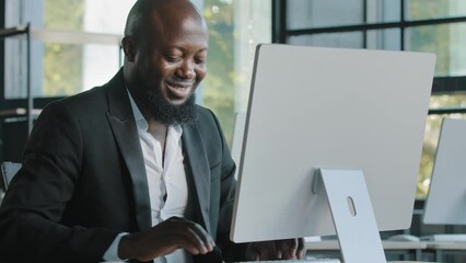 Middle-aged professional manager african adult millennial man work on computer business commerce online develop website programming data in internet emailing turns head at camera happy worker smiling
