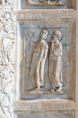 Close-up on carved sculptures decorating marble wall of catholic basilica in Pisa, representing two men interacting