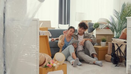 Wall Mural - Young happy Asia couple sit on sofa couch use digital tablet online shopping furniture from decoration store in living room at home. Husband wife move new house, Apartment Rent And Ownership Concept.