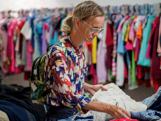 Woman choosing second hand clothes at the clothing store. Lifestyle.