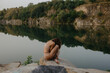 © Anastasia Mihaylova (Shpara)/Stocksy - Woman is sitting on the rocks in front of the lake in summer