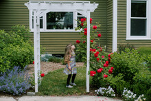 Little Girl In The Garden Looking At Red Roses