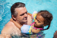 Father Holding His Young Child As They Sit In A Pool