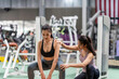 © crizzystudio - Female fitness instructor showing exercise progress to a young athletic woman at the gym and smiling cheerfully while exercising with his fitness coach and training.