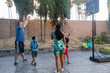 © ByLorena/Stocksy - Parents and children playing basketball in backyard