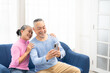 © Wongsakorn - Happy smiling asian senior couple sitting on sofa and using smartphone for online video call at home living room. Smiling mature Video Call Conference talk chat online concept.