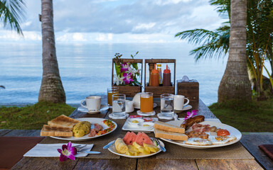Wall Mural - breakfast table on the beach with palm trees in Thailand. colorful breakfast with eggs and fruit