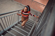 © Kay Abrahams/peopleimages.com - City, music and girl on stairs, phone in hand and listening to audio. Happy black woman with headphones streaming song, track or radio on smartphone in urban town, student freedom on weekend
