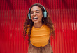 © Kay Abrahams/peopleimages.com - Urban, joy and woman with headphone music enjoying happy rhythm with bluetooth connection. Smile of latino girl listening to feel good streaming audio while resting at wall for leisure break.