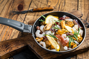 Cooking of fresh seafood mix in a skillet. Wooden background. Top view