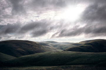 Wall Mural - Early morning sun breaking through the cloud over Coquetdale, the Cheviot Hills in Northumberland, England, UK.