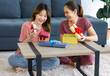 Asian young happy cheerful female teenager LGBTQ lesbian lover couple sitting smiling together on carpet floor in living room holding exchanging opening wrapped present gift box celebrating festival