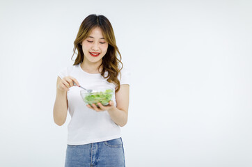 Isolated cutout studio shot of Millennial Asian young happy female teenager model in casual outfit standing smiling holding fresh organic salad glass bowl and red tomato on fork on white background