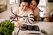 © Maskot - Woman using smart phone on table while embraced by daughter at home