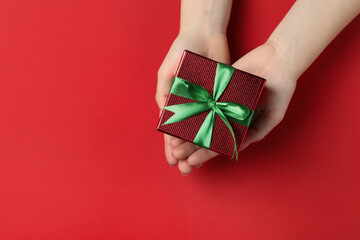 Wall Mural - Woman holding beautifully wrapped Christmas gift box on red background, top view. Space for text